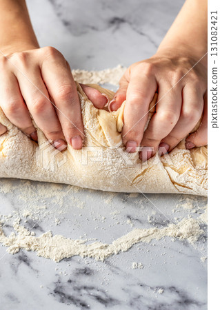 Women's hands kneading dough on white marble table. Making cinnamon rolls process. Cinnabon preparation 131082421