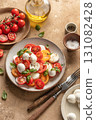 Caprese salad with sliced tomatoes, mozzarella, basil, olive oil on brown textured background 131082428
