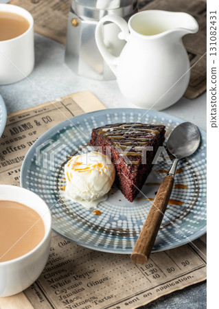 A piece of chocolate brownie cake on blue plate served with a scoop of ice cream and caramel topping with coffee A piece of chocolate brownie cake on blue plate served with a scoop of ice cream and caramel topping with coffee 131082431