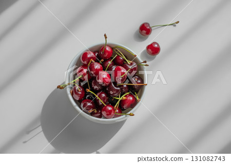 Bowl with fresh red cherry on white background with sunny light and shadows. Bowl with fresh red cherry on white background with sunny light and shadows. 131082743