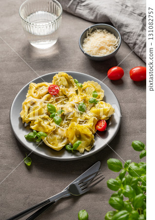 Tortellini pasta with parmesan, pesto and basil in a plate on a dark background with glass of water Tortellini pasta with parmesan, pesto and basil in a plate on a dark background with glass of water 131082757