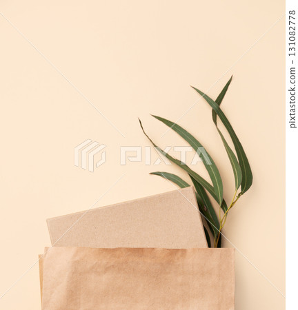 Kraft paper bag with notebook and green leaves inside, minimalistic style on beige background Kraft paper bag with notebook and green leaves inside, minimalistic style on beige background 131082778