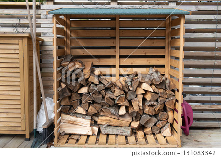 Wooden firewood storage near the house, next to it are garden tools. Wooden firewood storage near the house, next to it are garden tools. 131083342