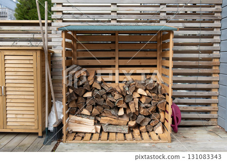 Wooden firewood storage near the house, next to it are garden tools. 131083343