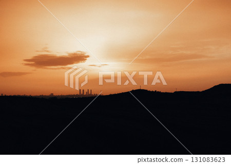 Beautiful sunset paints the sky with vibrant orange and casting warm glow over the landscape. A breathtaking sunrise skyline with orange hues and warm glow over the silhouetted land and horizon. 131083623