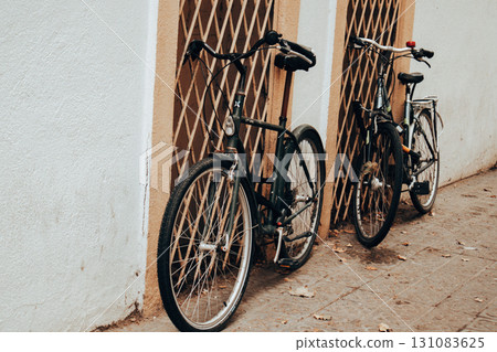 Two vintage bicycles lean against a textured wall and ornate metal grate. The bikes have a classic design and the scene has nostalgic aesthetic. Urban lifestyle, eco transport and sustainable living. Two vintage bicycles lean against a textured wall and ornate metal grate. The bikes have a classic design and the scene has nostalgic aesthetic. Urban lifestyle, eco transport and sustainable living. 131083625