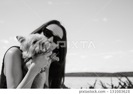 A young brunette woman kisses her adorable Yorkshire terrier dog in a moment of affection. A woman in sunglasses kisses her small doggy 131083628