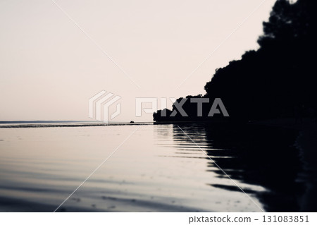 Silhouette of a boat on the lake at dusk with reflections and calm waters A tranquil seascape with a reflective lake mirroring the sky and silhouetted trees. A small boat glides across the water. 131083851