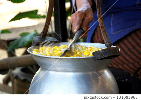 The hands of an old woman are boiling silkworm nests in a pot to separate them into fibers to make silk thread. 131083965