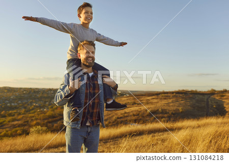 Portrait of little child boy sitting on fathers shoulders enjoying sunset and nature outdoors. 131084218