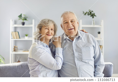Portrait of a happy senior couple standing at home hugging and looking cheerful at camera. 131086713