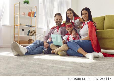 Happy family in red super hero costumes using laptop together sitting on the floor at home. Happy family in red super hero costumes using laptop together sitting on the floor at home. 131088117