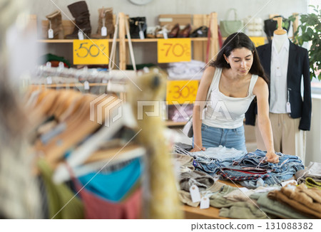 Young woman customer making choice and elect pants in store Young woman customer making choice and elect pants in store 131088382