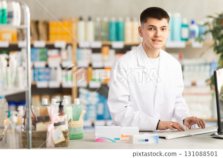 Professional young man pharmacist standing at prescription counter and working on computer, stocktaking medicines at pharmacy shop Professional young man pharmacist standing at prescription counter and working on computer, stocktaking medicines at pharmacy shop 131088501