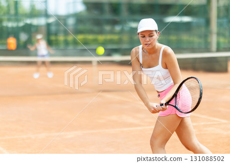 Concentrated sporty girl with tennis racquet and ball in her hands standing and ready to play match standing Concentrated sporty girl with tennis racquet and ball in her hands standing and ready to play match standing 131088502