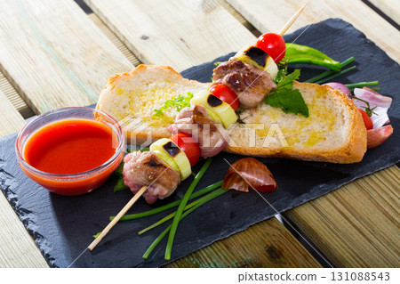 Baked shashlik of lamb with onion and tomatoes served with ketchup and bread 131088543