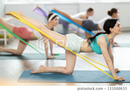 Girl leads class women, standing on all fours, performing exercises with wide elastic skip rope 131088633