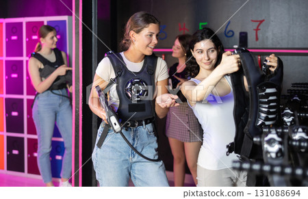 Girls try on a matching vest for playing laser tag in dark room 131088694