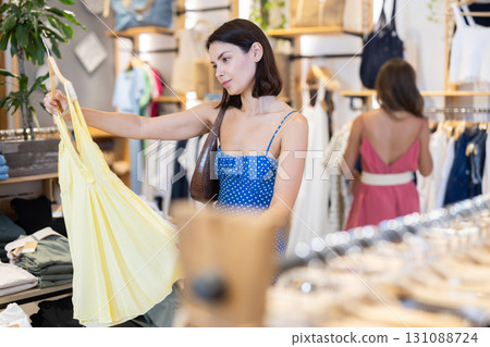 Two female shoppers carefully choosing clothes - dress, jeans, skirts and other clothes in clothing store Two female shoppers carefully choosing clothes - dress, jeans, skirts and other clothes in clothing store 131088724