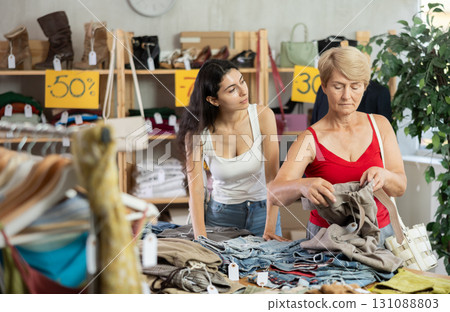 Woman customer with senior mother making choice and elect pants in store 131088803