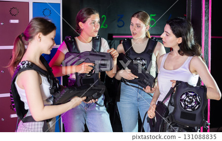 Group of girls in laser tag vests with rifles in their hands are discussing the rules of game of laser tag Group of girls in laser tag vests with rifles in their hands are discussing the rules of game of laser tag 131088835