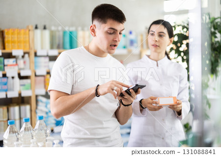 Young man with phone is shopping in pharmacy, girl employee offer help and support 131088841