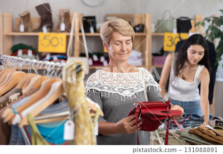 Senior woman customer elect leather handbag in store. Female client choosing something in background Senior woman customer elect leather handbag in store. Female client choosing something in background 131088891