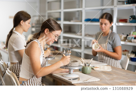 Woman teacher and students sculpt and paint ceramics 131088929