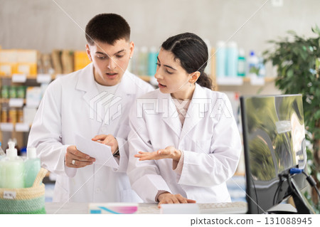 Two male and female pharmacists attentively stocktaking medicines with computer at pharmacy shop Two male and female pharmacists attentively stocktaking medicines with computer at pharmacy shop 131088945