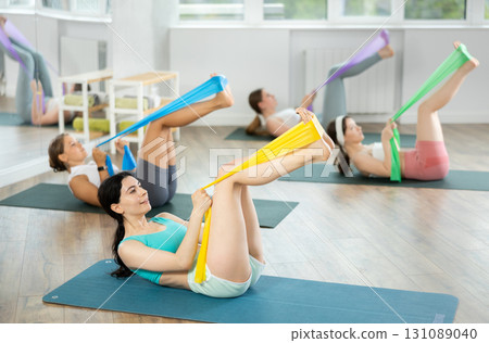 Girl lying and perform variety of exercises to strengthen muscles of press with wide resistance band 131089040
