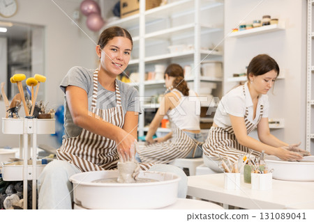 Three young women sits near potter wheel and makes clay crafts 131089041