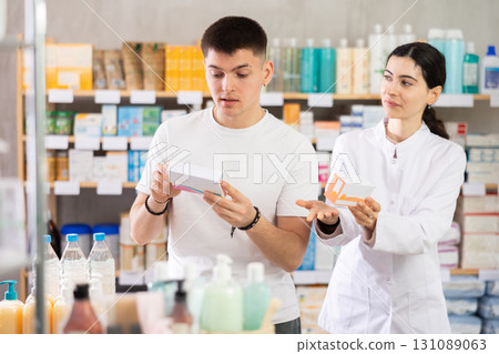 Guy chooses pills in modern pharmacy. Female pharmacist helps with choosing medicine 131089063