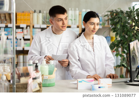 Two male and female pharmacists attentively stocktaking medicines with computer at pharmacy shop Two male and female pharmacists attentively stocktaking medicines with computer at pharmacy shop 131089077