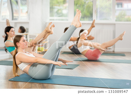 Young female participant working out Paripurna Navasana, boat pose with students group 131089547