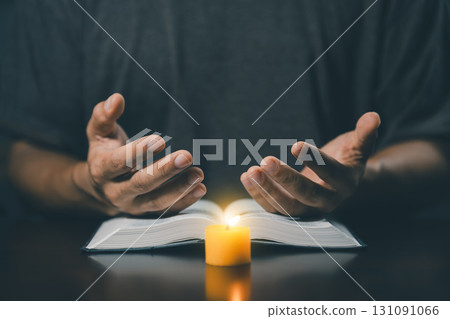 Christian man worship. Hands folded in prayer on a Holy Bible in home concept for faith. Spirituality and religion. Man praying on holy bible with candle light. Man hand with Bible praying. Christian man worship. Hands folded in prayer on a Holy Bible in home concept for faith. Spirituality and religion. Man praying on holy bible with candle light. Man hand with Bible praying. 131091066