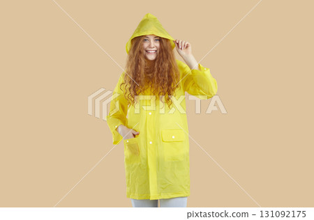 Smiling curly young redhead girl in yellow raincoat looking at camera on beige background. 131092175