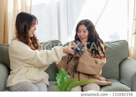 Winter day brings cheerful women friends home showing warm friendship exchanging practical gifts like gloves enjoying cozy comfortable indoor winter celebration fostering close bond. 131092356