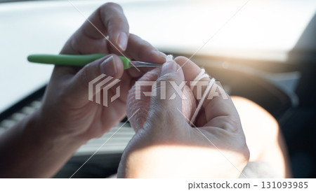 Woman hands are knitting a crocheted blanket. Pink yarn and green handle crochet. Leisure activities while sitting in the car with warm light. 131093985