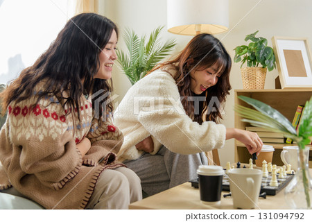 Winter day friends enjoy home leisure, cozy home activities, fostering friendship, playing chess, warm drinks, making memories during cold winter days indoors. 131094792