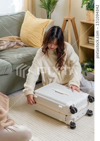 Winter friends home, young woman carefully packing home travel suitcase, friendship preparation for exciting vacation trip, cozy winter leisure time, enjoying relaxation indoors. Winter friends home, young woman carefully packing home travel suitcase, friendship preparation for exciting vacation trip, cozy winter leisure time, enjoying relaxation indoors. 131094842