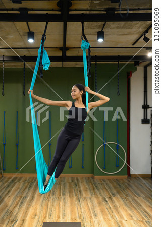 Female athlete standing confidently with aerial yoga swing, focusing on strength and balance training 131095069
