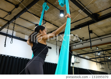 Female athlete practicing aerial yoga, gripping silk fabric with strength and focus 131095070