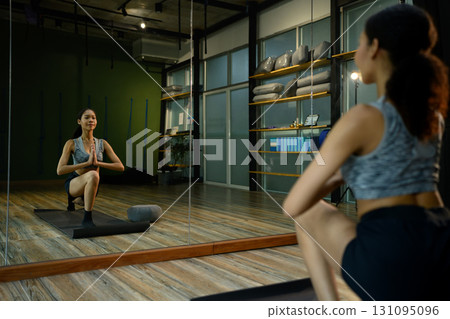 Woman in sportswear doing yoga exercise indoors, stretching and strengthening body with calm expression Woman in sportswear doing yoga exercise indoors, stretching and strengthening body with calm expression 131095096