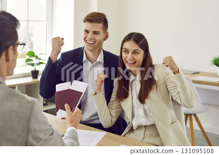 Happy couple sitting in travel agency going in vacation receiving passports with tickets 131095108
