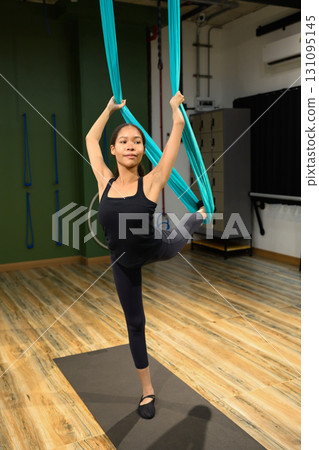 Woman practicing aerial yoga pose with hammock, balancing gracefully in a fitness studio 131095145