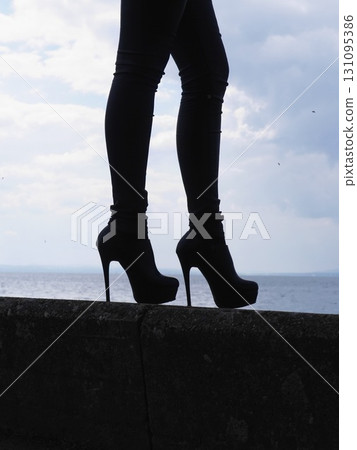 Woman wearing black high heels is standing on a ledge overlooking the ocean Woman wearing black high heels is standing on a ledge overlooking the ocean 131095386