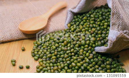 Close-up of raw mung beans spilling from a burlap sack with a wooden spoon on wooden background. Suitable for concepts of organic farming 131095559