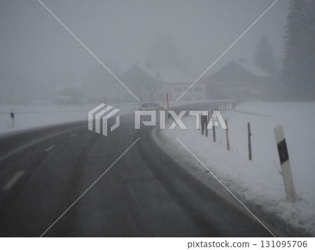Snowy road with a car driving down it 131095706