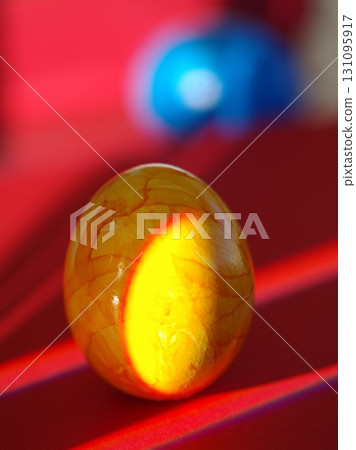A yellow egg with a shadow on it is on a red surface A yellow egg with a shadow on it is on a red surface 131095917