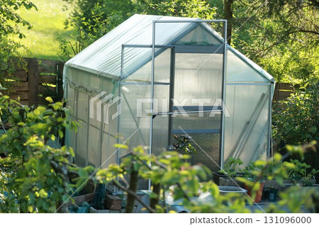 A greenhouse is sitting in a garden with a fence behind it 131096000